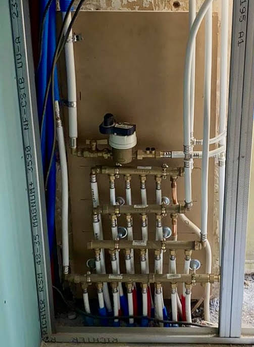 Artisan plombier chauffagiste installant un réseau de plomberie avec collecteurs